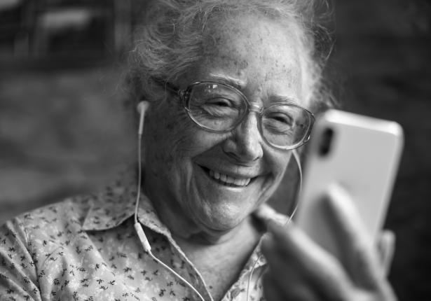 Greyscale of older woman listening to book on smartphone.