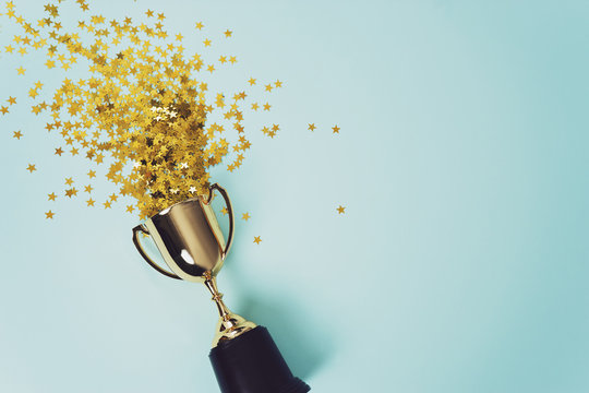 Un trophée débordant de confettis or sur un fond bleu.