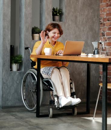 femme dans un fauteuil roulant saluant les gens lors d'une réunion virtuelle sur un ordinateur